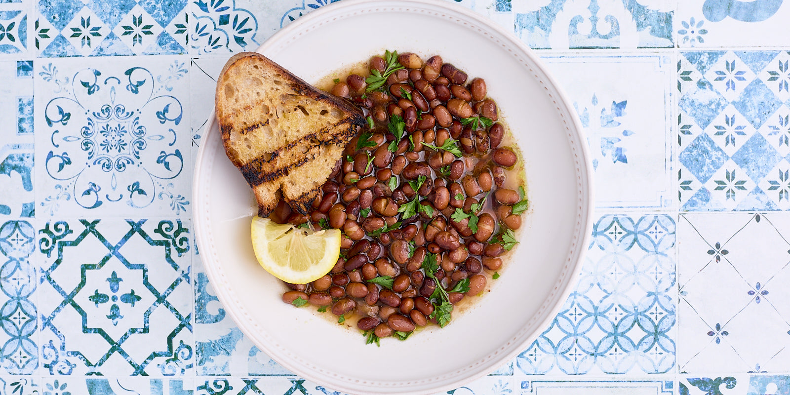 brothy beans in a white bowl on a blue tile counter