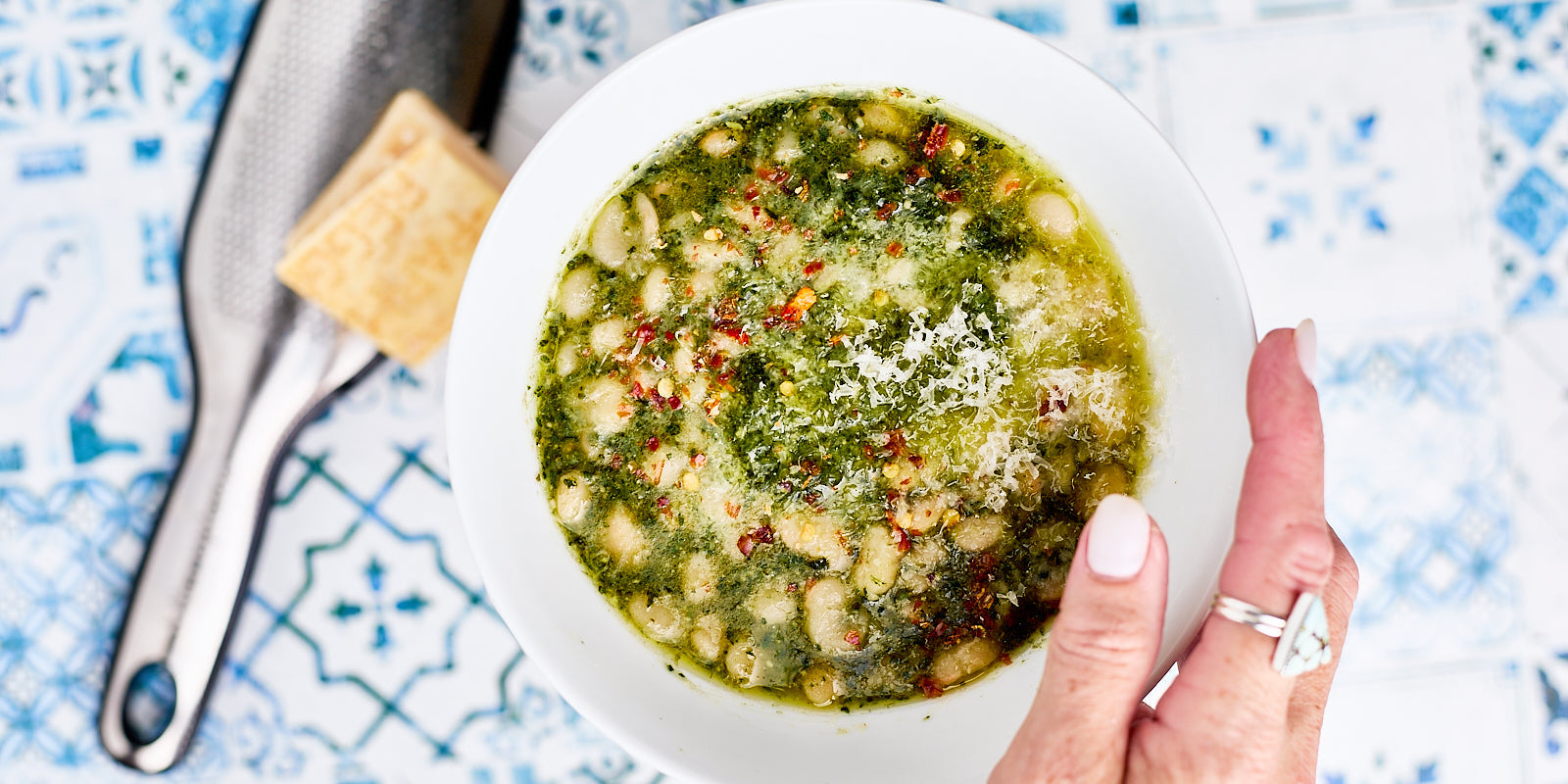bowl of white beans swimming in a bright green pesto and topped with parmesan and chili flakes
