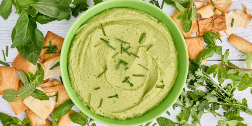 bowl of vibrant green goddess white bean dip surrounded by herbs