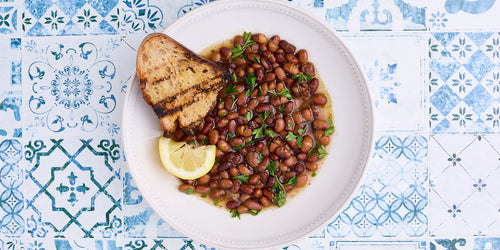 brothy beans in a white bowl on a blue tile counter