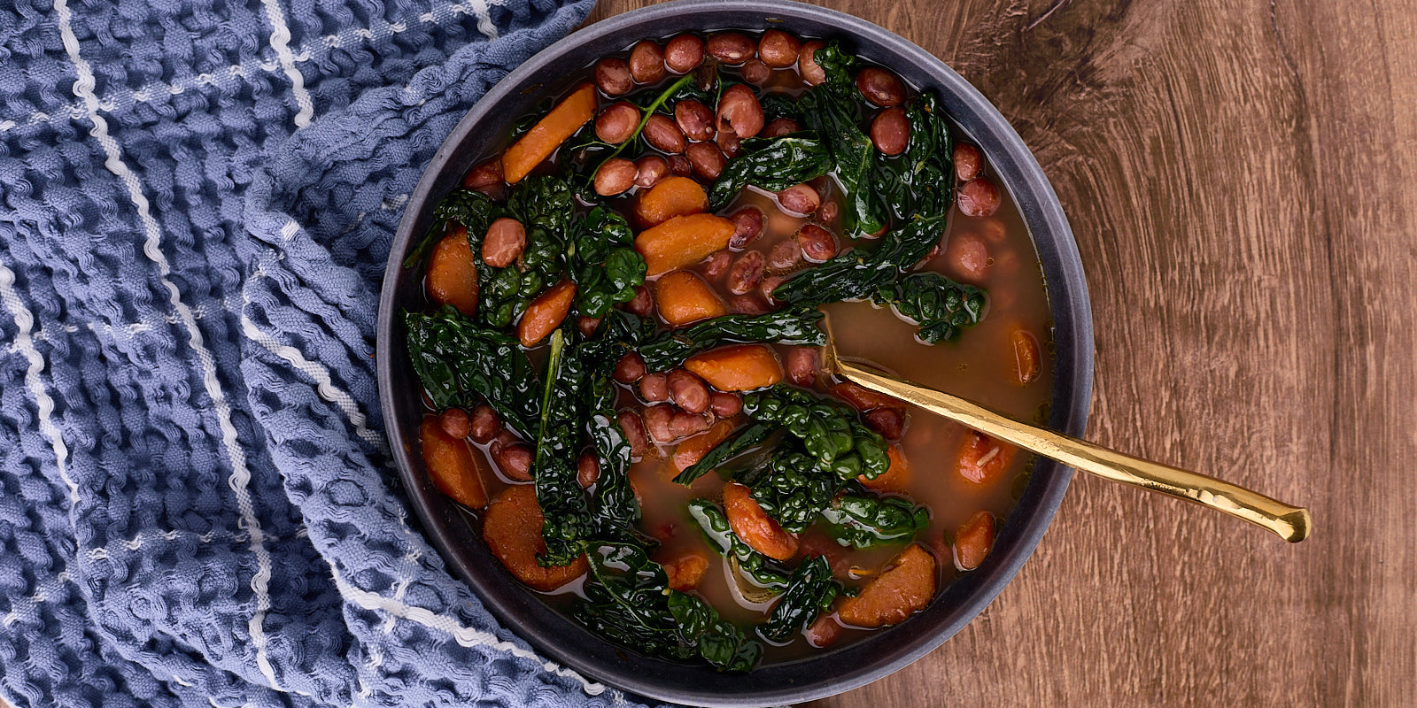 bowl of beans with kale and carrots on wood surface with blue and white striped towel