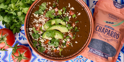 black bean soup topped with avocados next to a bag of heirloom black beans