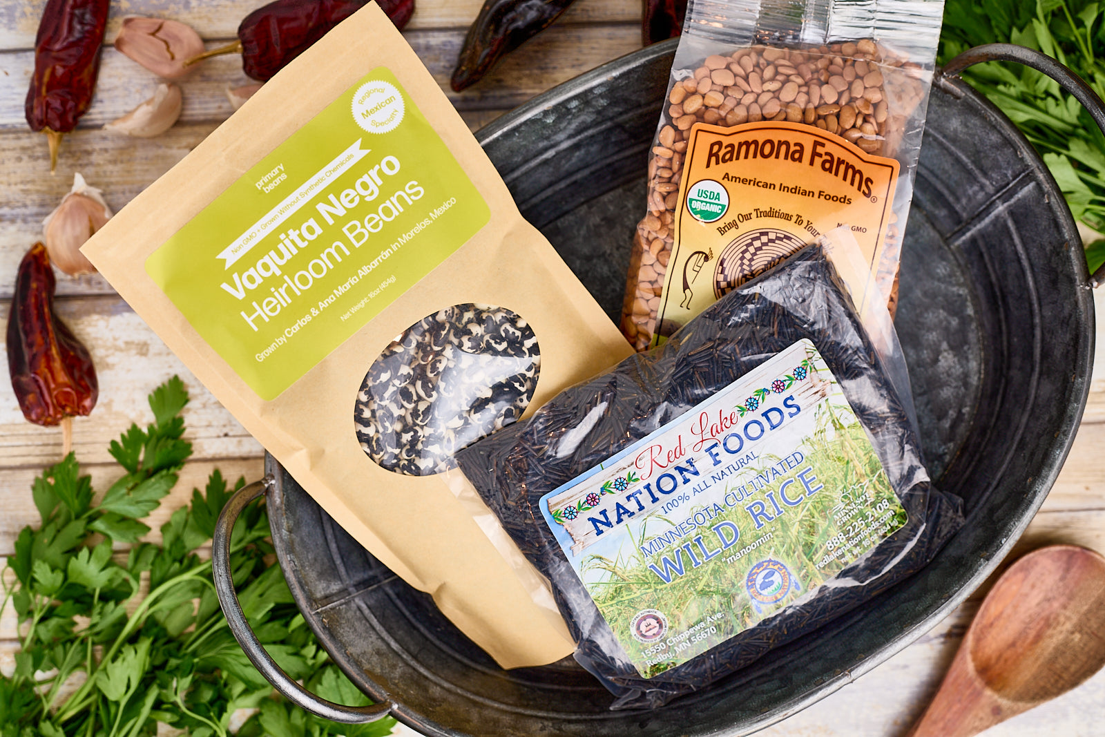 Heirloom beans and ancient grains in a farm bucket surrounded by herbs and chilis