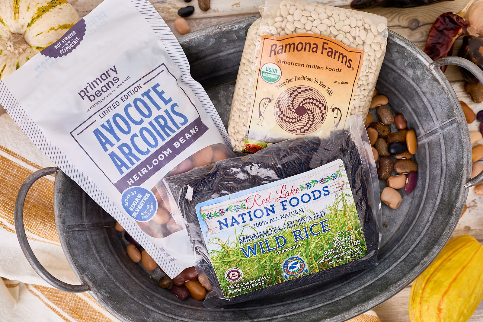 ayocote arcoiris, white tepary beans and wild rice on a counter with decorative beans and vegetables around them. 