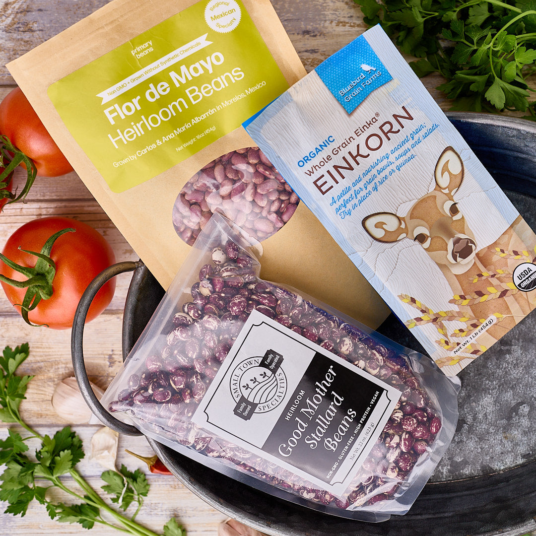 Three packages of beans on a wooden surface with tomatoes and herbs.