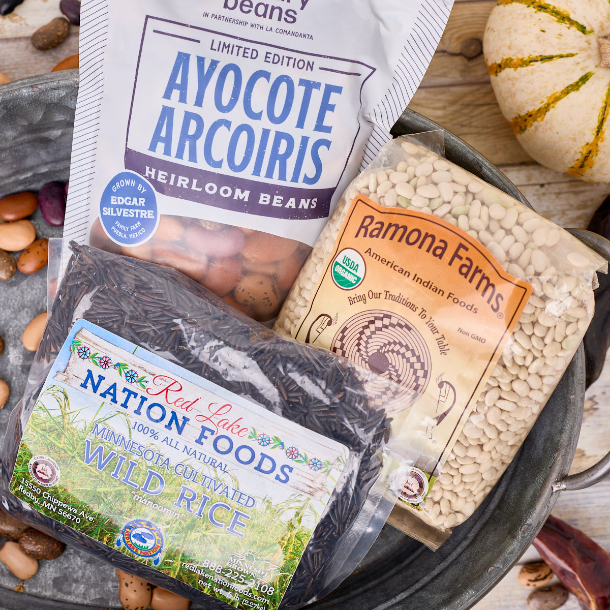 Ayocote Arcoiris beans, tepary beans and wild rice on a wood counter with decorative beans and vegetables