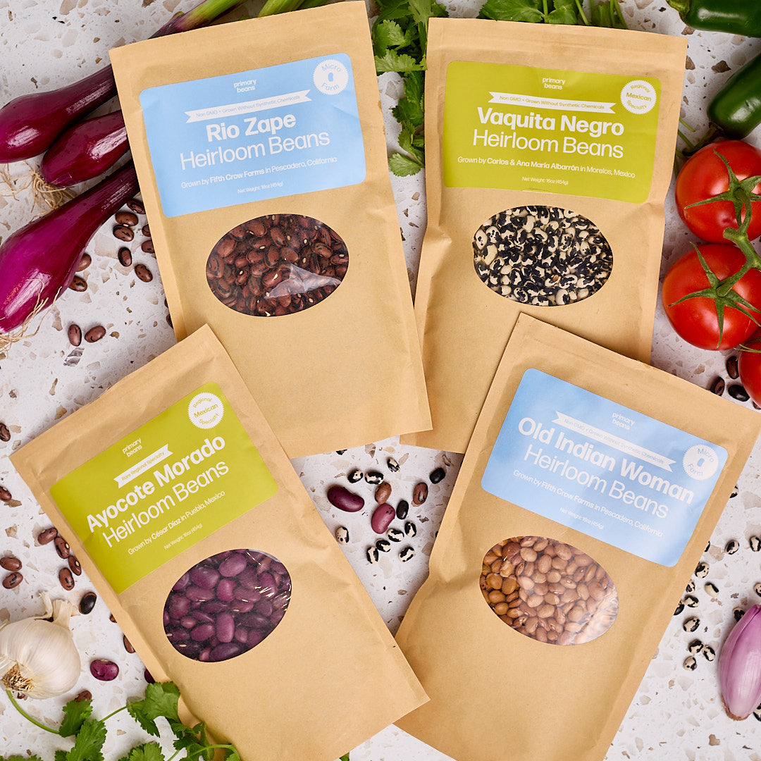 Four packages of heirloom beans with labels on a background of vegetables.