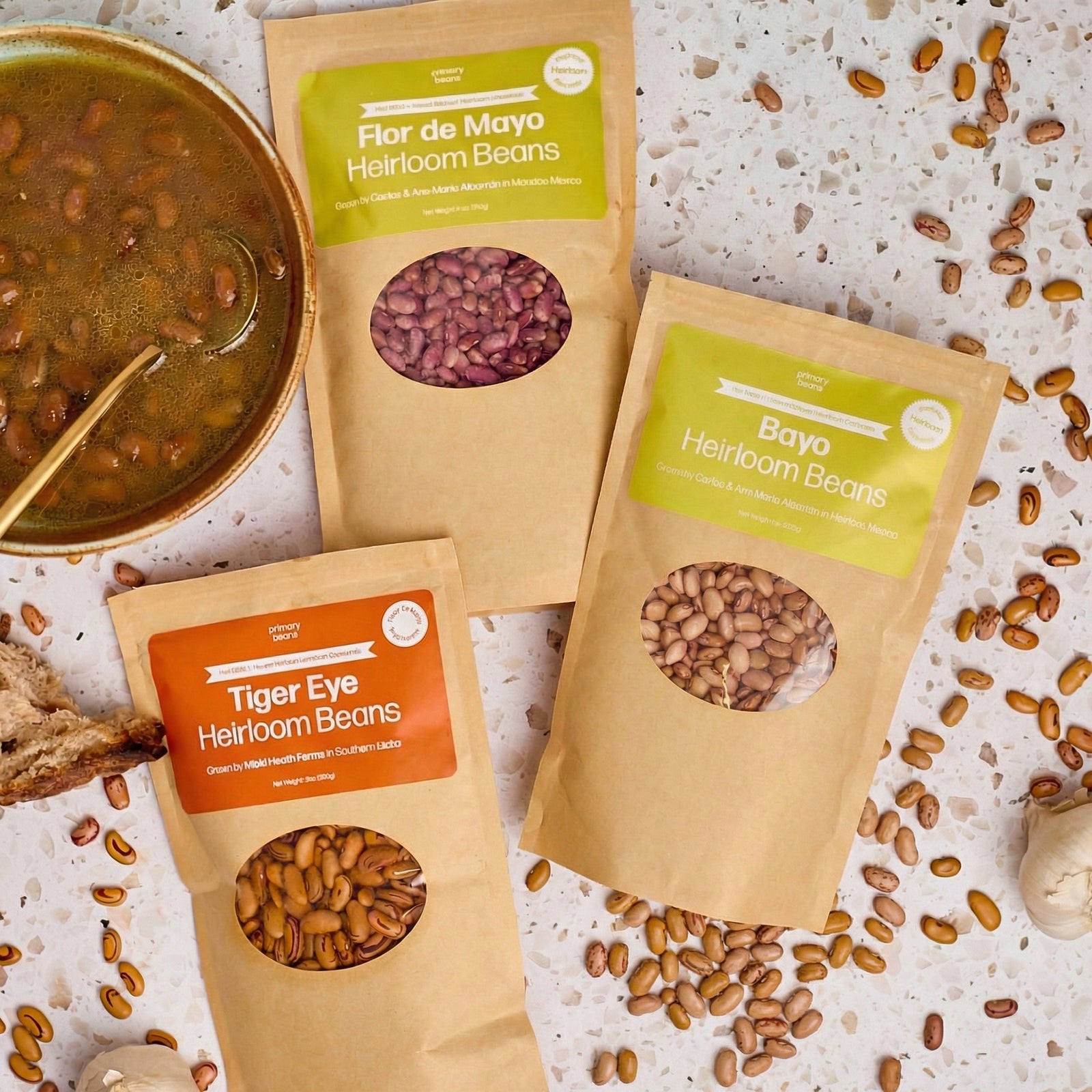 Three packages of heirloom beans with visible contents on a textured surface.