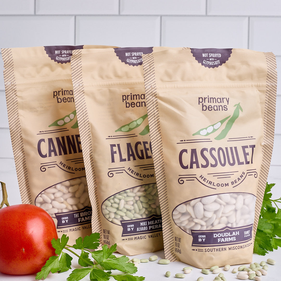 3 bags of dried beans surrounded by decorative herbs and tomatoes 