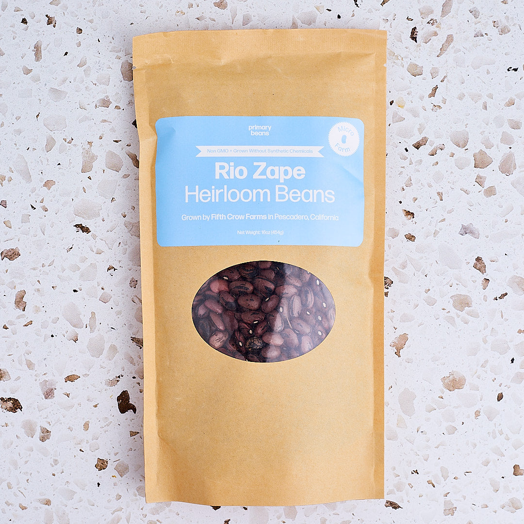 Kraft paper package with a window showing Rio Zape Heirloom Beans on a textured surface.